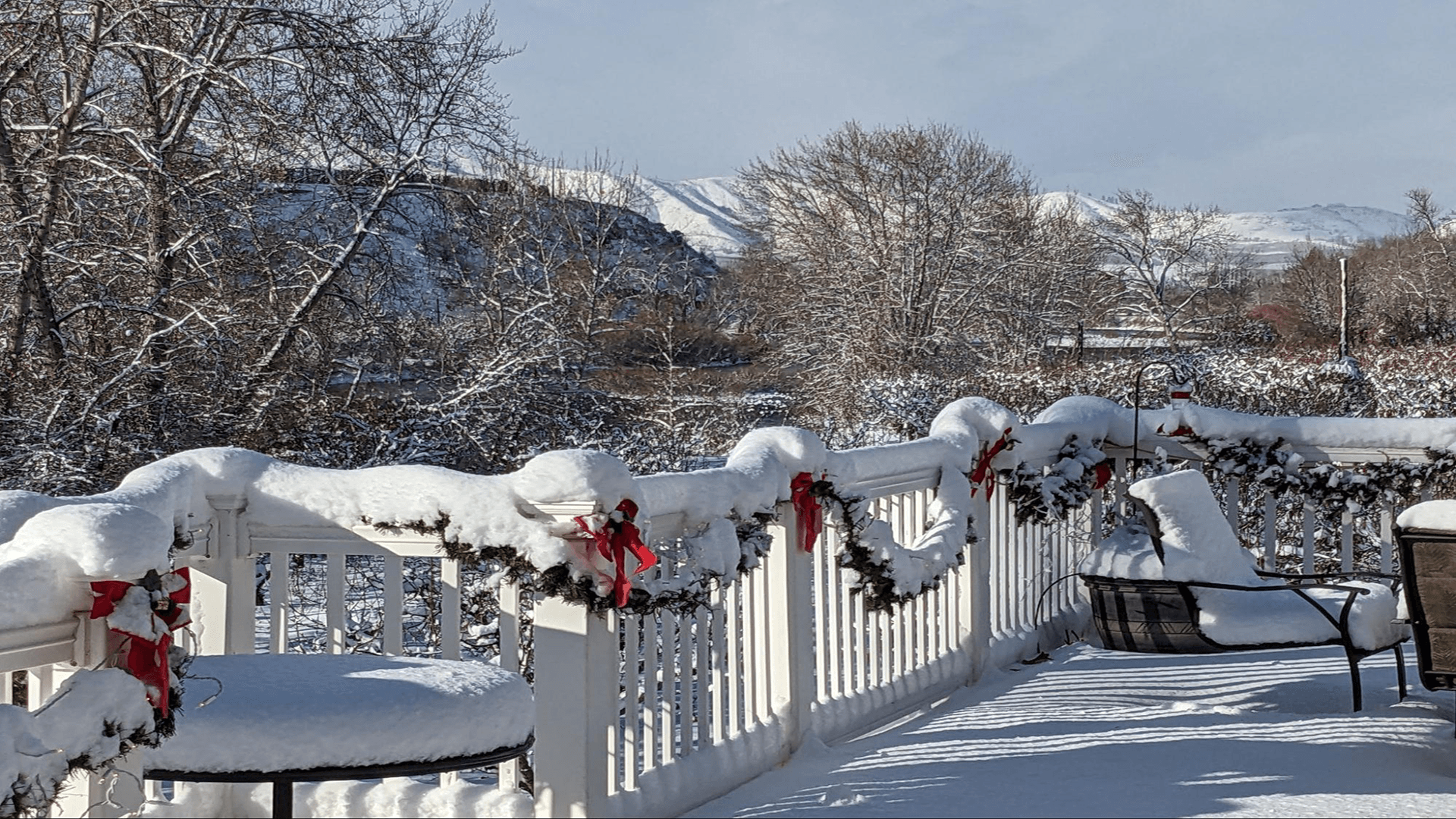 A snowy deck adorned with garlands and ribbons overlooks a winter landscape.
