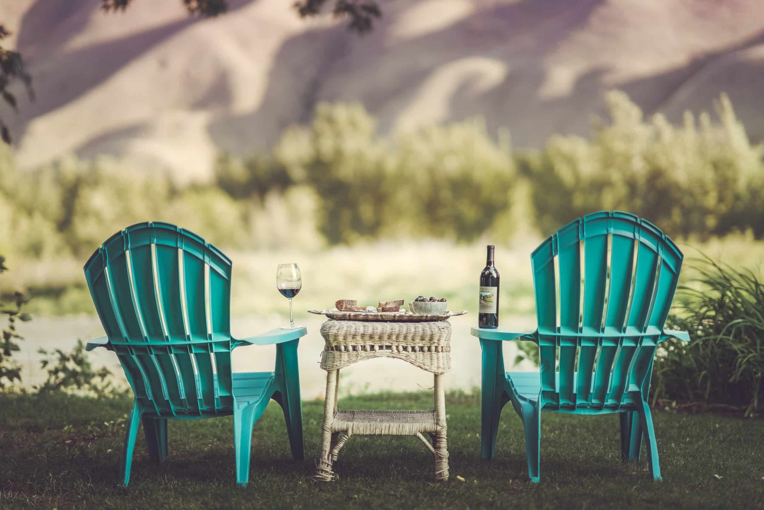 Two turquoise chairs facing a river, with a table set for wine and snacks.