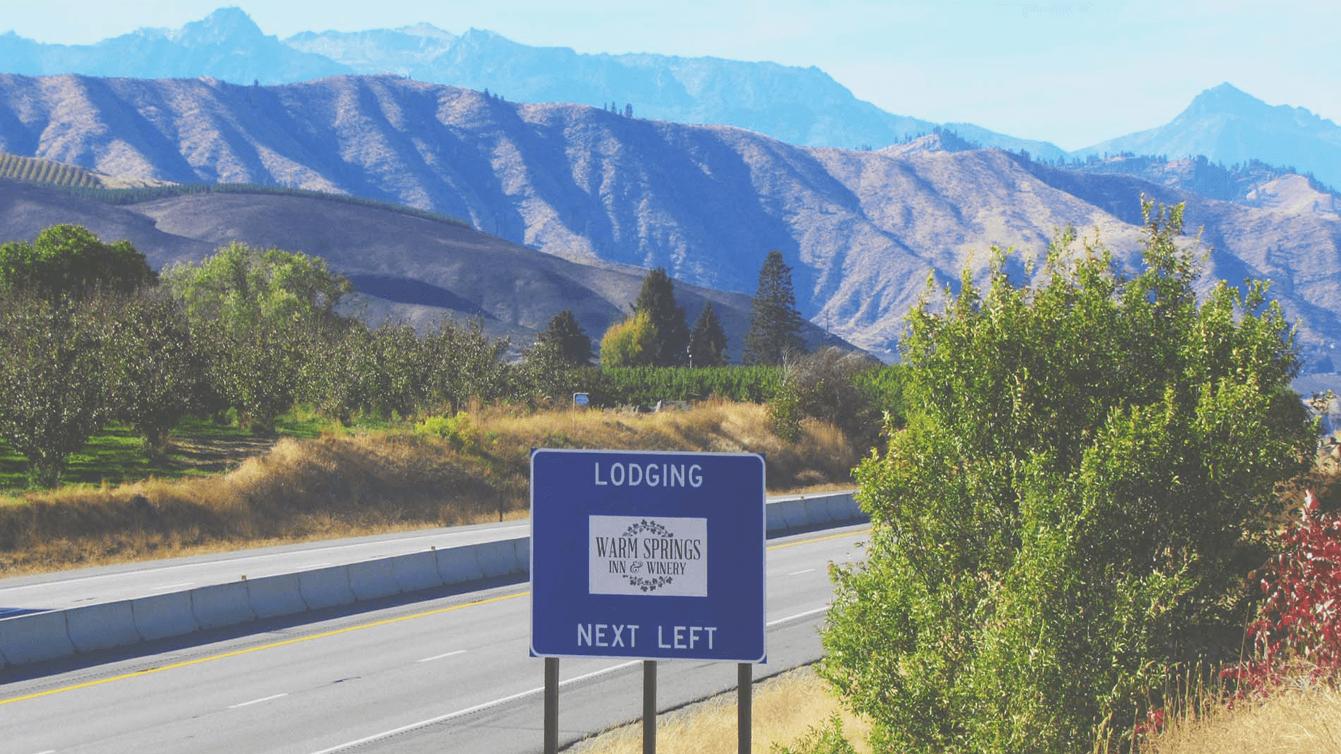 A blue roadside sign indicating "Lodging" at "Warm Springs Inn & Winery" with mountains in the background.