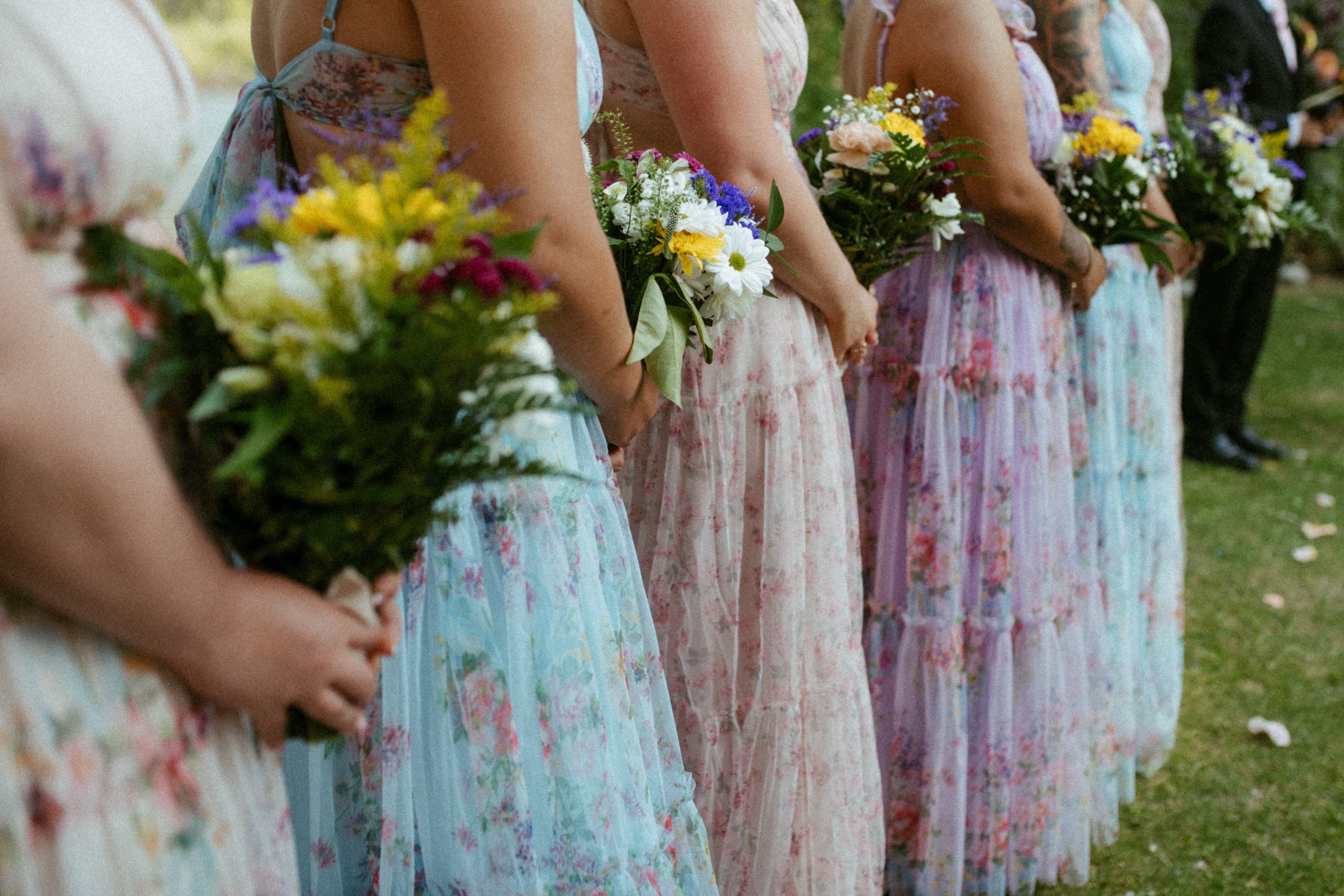 A lineup of bridesmaids in flowy floral dresses holding bouquets of flowers.