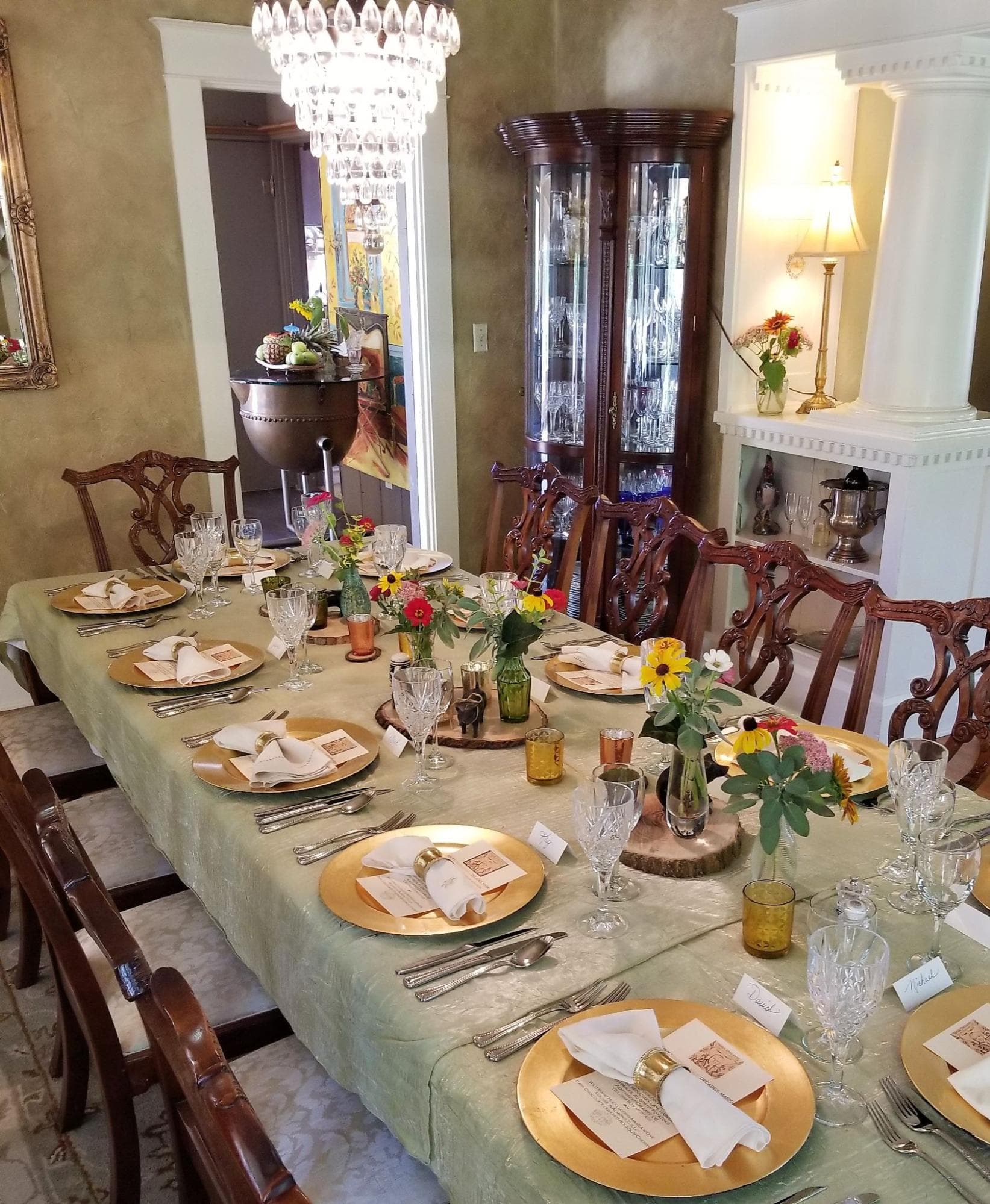 A beautifully set dining table adorned with flowers, elegant dinnerware, and sparkling crystal under a chandelier.