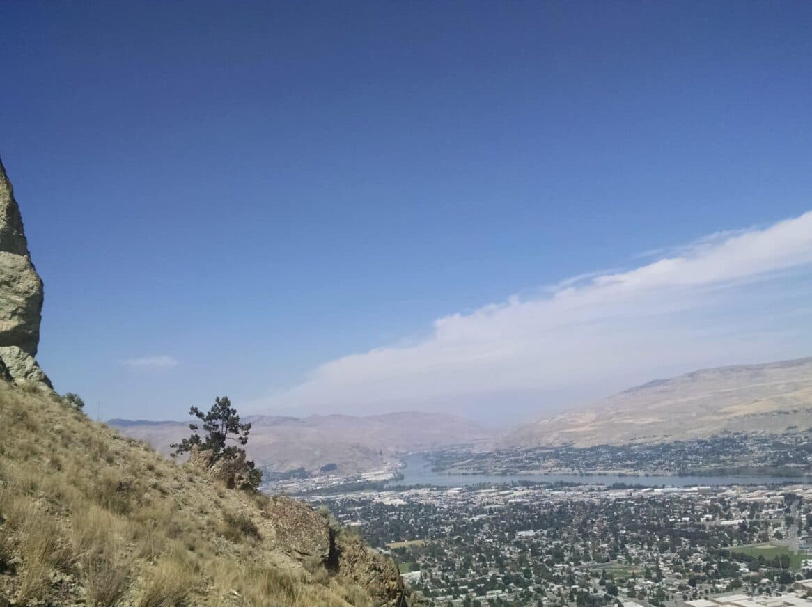 A panoramic view of a valley with hills and a river under a clear blue sky.