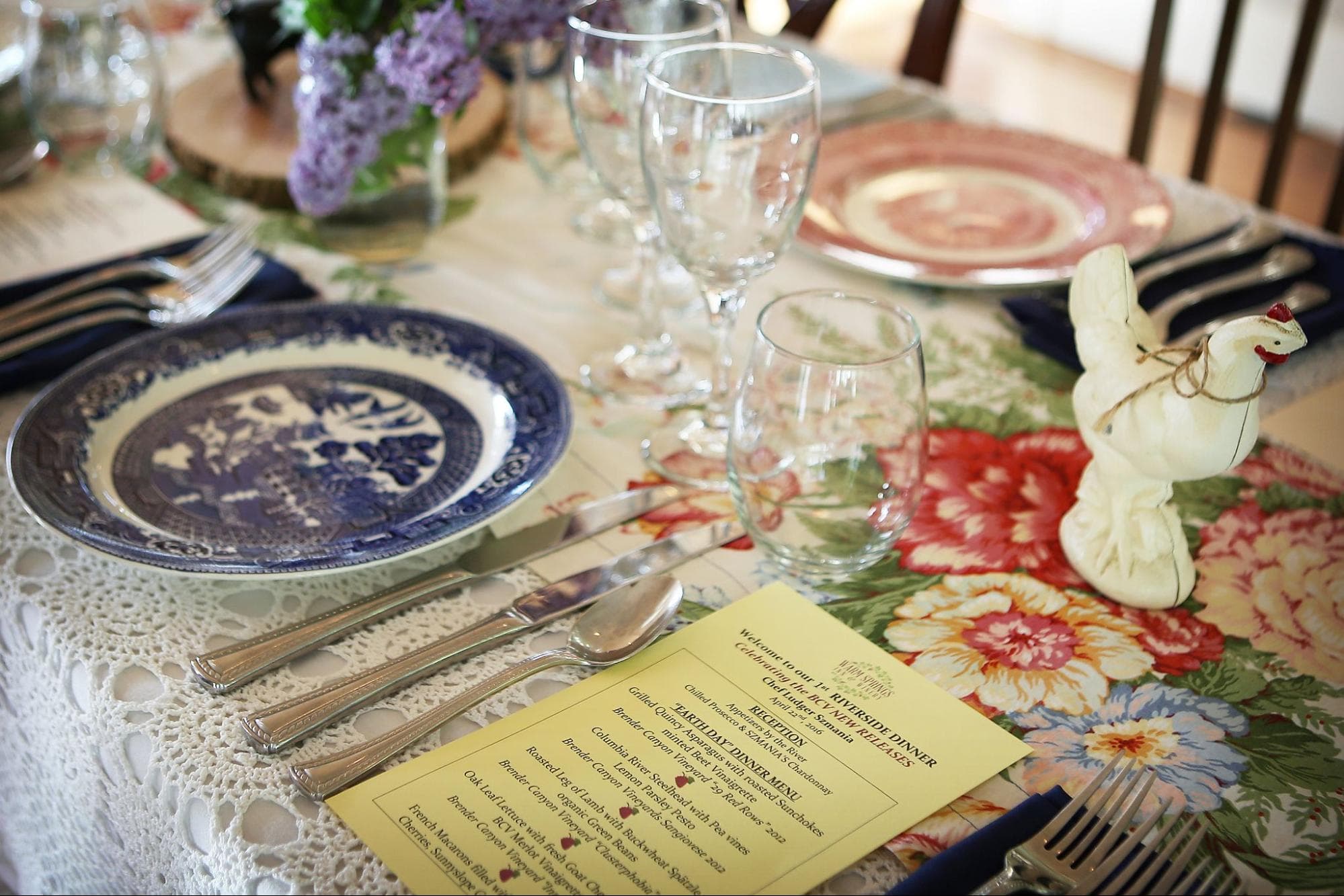 A beautifully set dining table with floral decorations, colorful plates, and a menu.