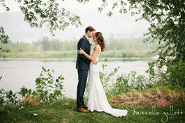 A couple shares a romantic moment by a river, dressed for their wedding.