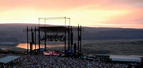 A large crowd gathers at an outdoor concert during a colorful sunset.
