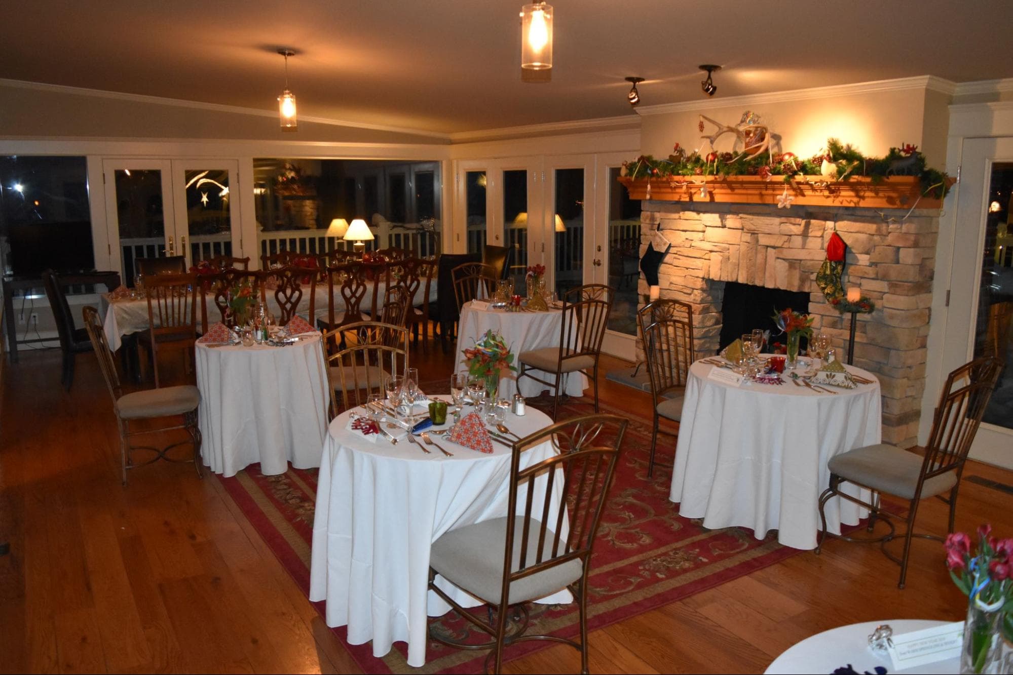 A cozy dining room with elegantly set tables and a stone fireplace, decorated for the holidays.