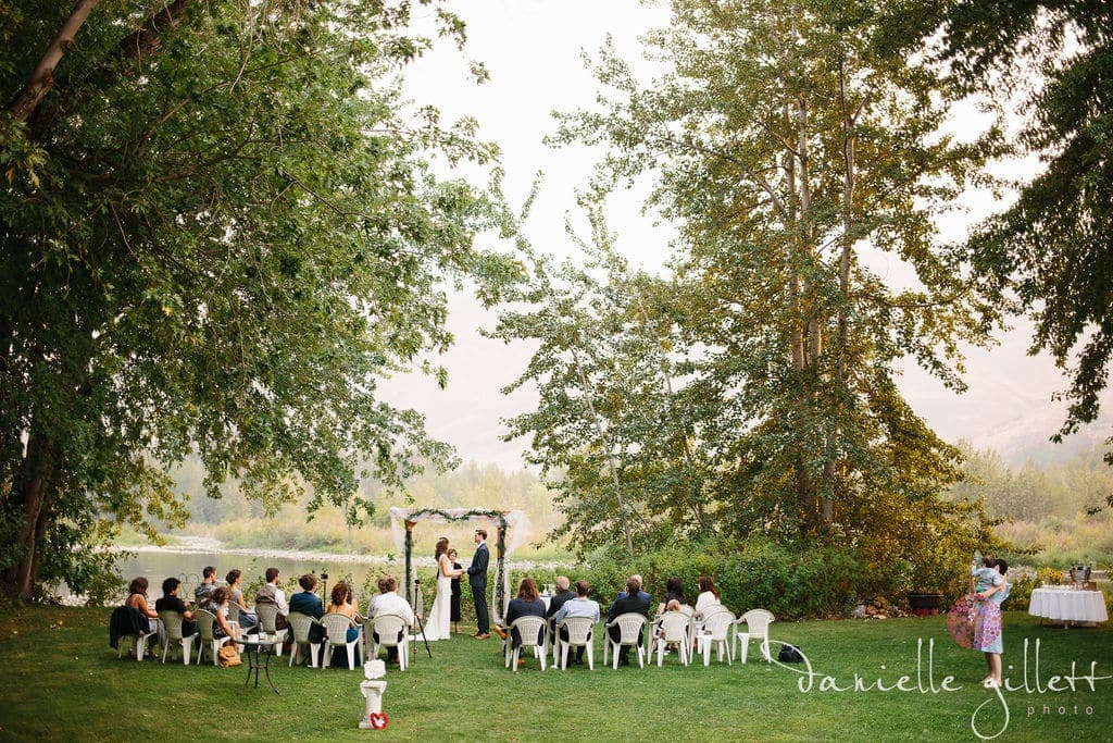 A couple exchanges vows at an outdoor wedding ceremony surrounded by guests and nature.