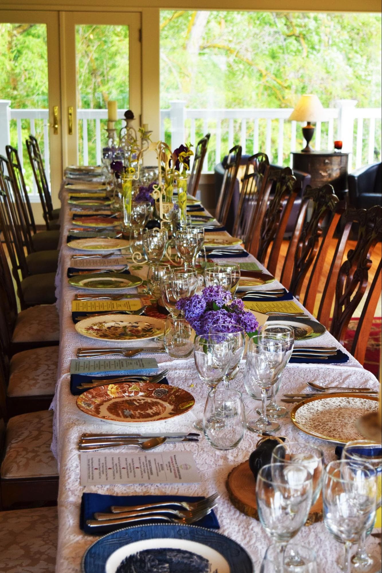 A beautifully set long dining table adorned with flowers, elegant dishware, and glassware, ready for a gathering.