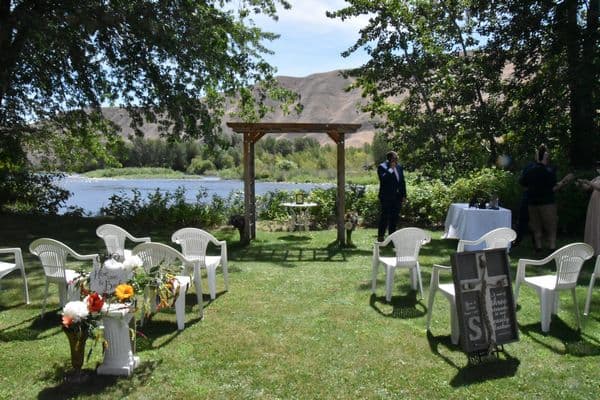 A scenic outdoor wedding setup by a river, featuring white chairs and an arch.