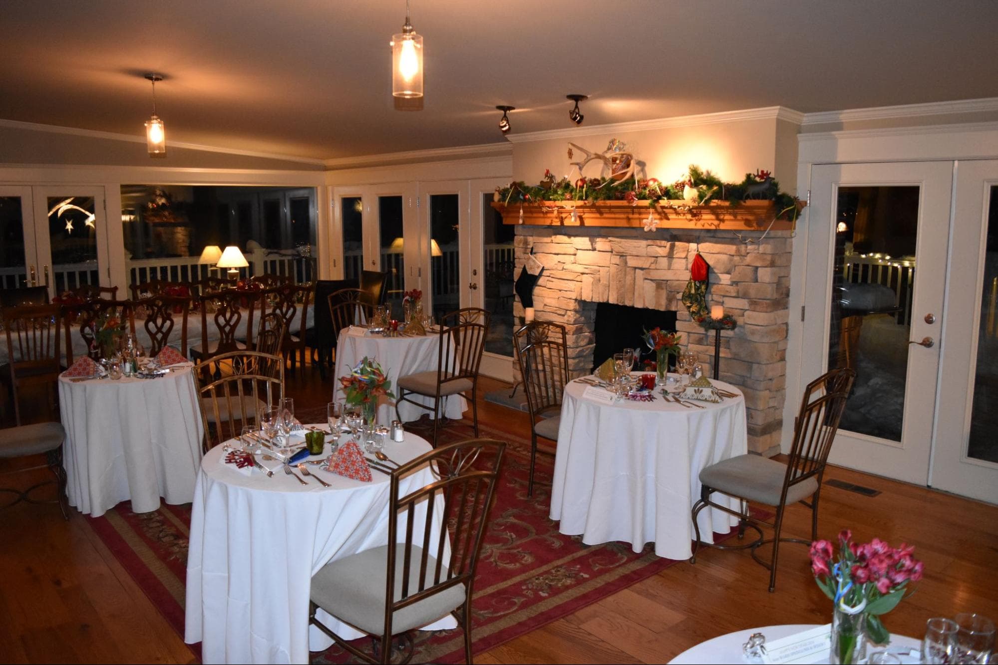 A warmly lit dining room with elegantly set tables and a stone fireplace decorated for the holidays.