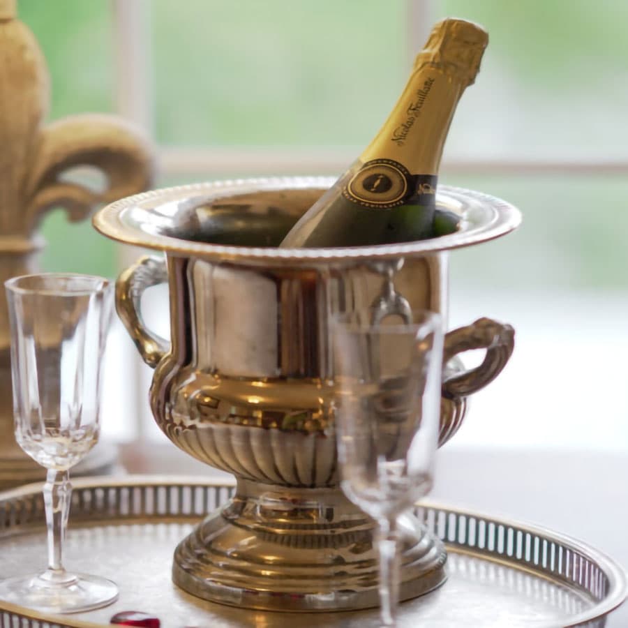 A champagne bottle is cooling in a silver ice bucket beside elegant fluted glasses.