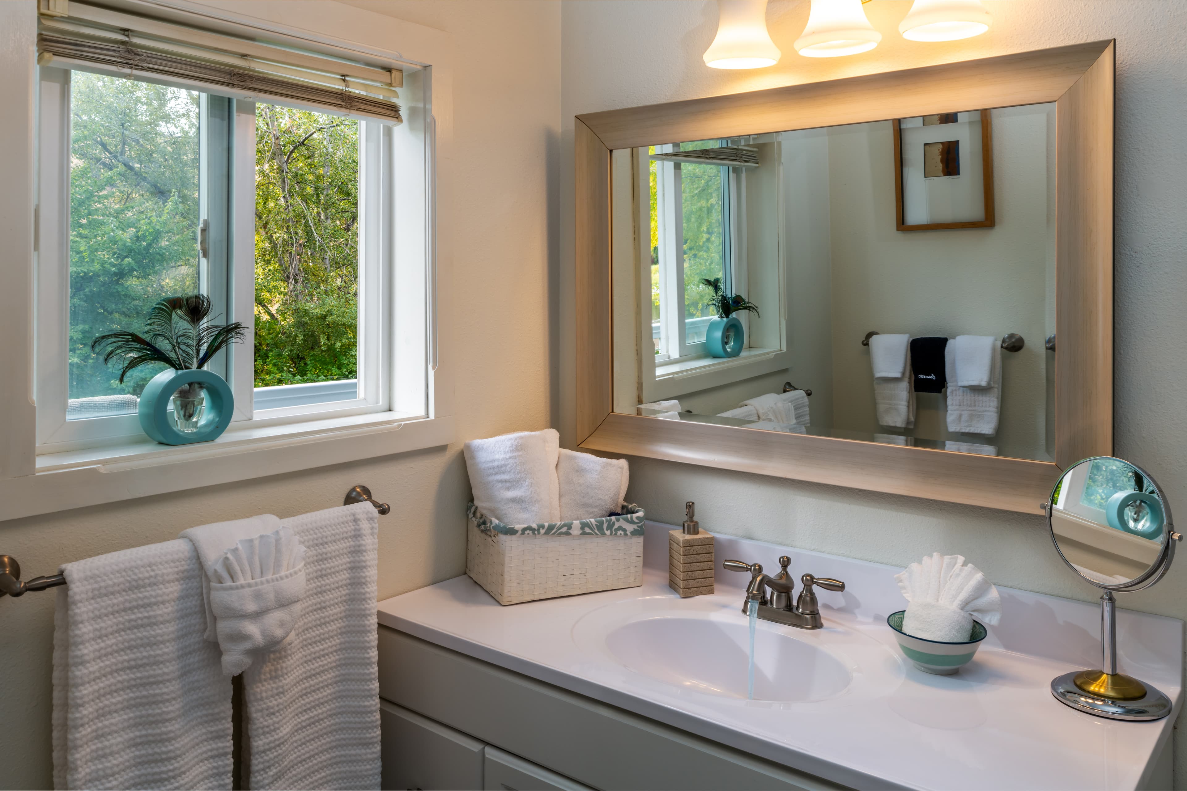 Bright bathroom with a window, mirror, sink, and neatly arranged towels.