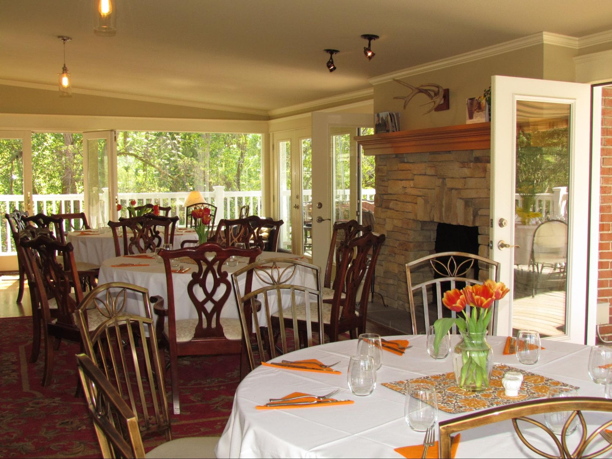 A bright dining area with elegantly set tables and a view of greenery through large windows.