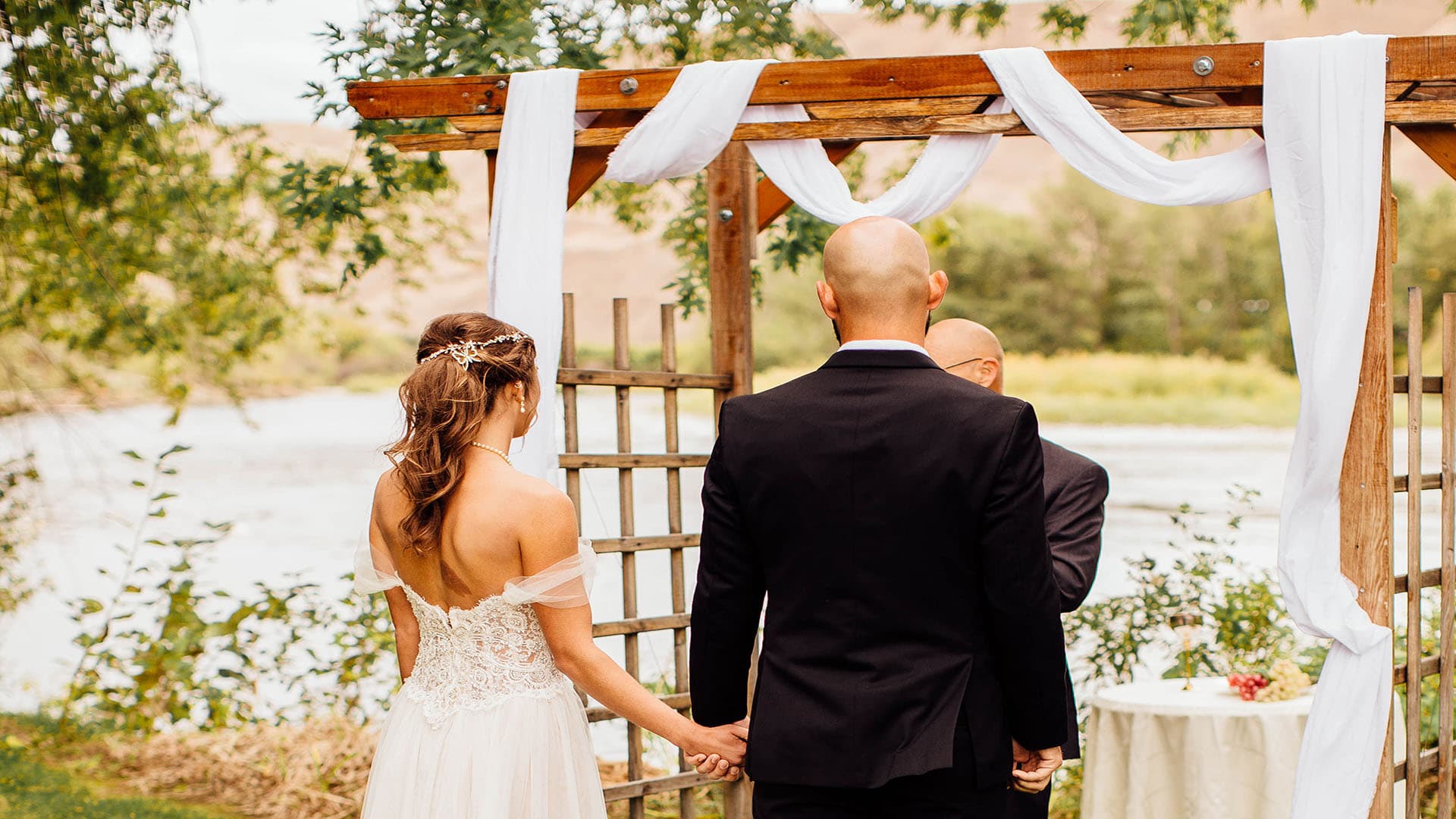 A bride and groom hold hands during their outdoor wedding ceremony by a river.