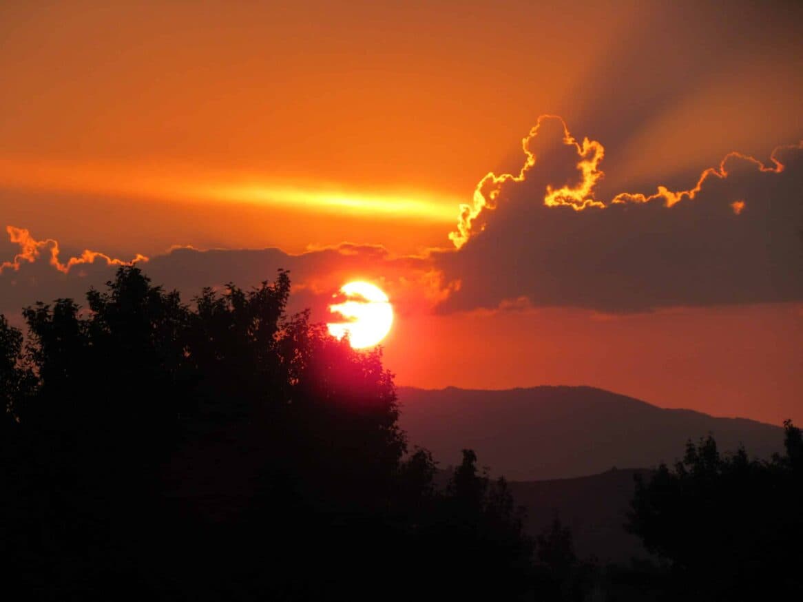 A vibrant sunset casting orange hues over silhouetted mountains and trees.