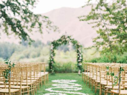 Flower petals line the grassy isle to down to a wedding altar and is surrounded by rustic wooden chairs.